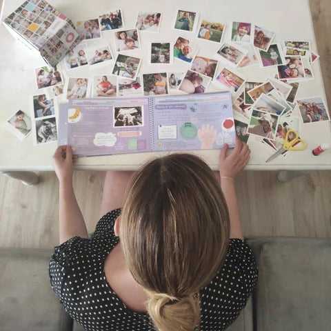 Mujer revisando un diario de embarazo con fotos de ultrasonidos y recuerdos familiares en una mesa.